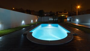 A rectangular swimming pool with a light blue interior, surrounded by a wooden deck and a low white wall.
