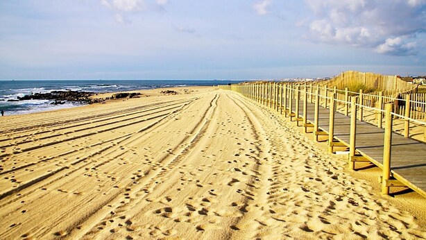 A sandy beach with a wooden boardwalk leading to the ocean.