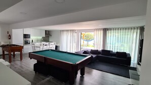 A modern living room with a pool table, a sofa, and a dining area with a table and chairs.