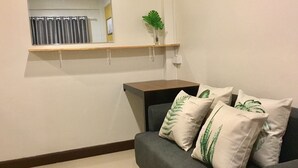 Una sala de estar con un sofá gris, un estante de madera arriba y una pequeña planta en maceta.