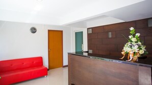 Una zona de recepción con un mostrador de madera, un sofá rojo y un reloj en la pared.