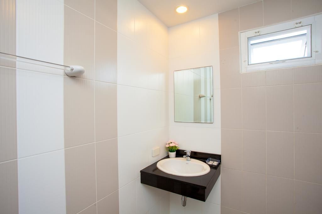 A modern bathroom with white tiles, a black sink vanity, a mirror, and a small potted plant.