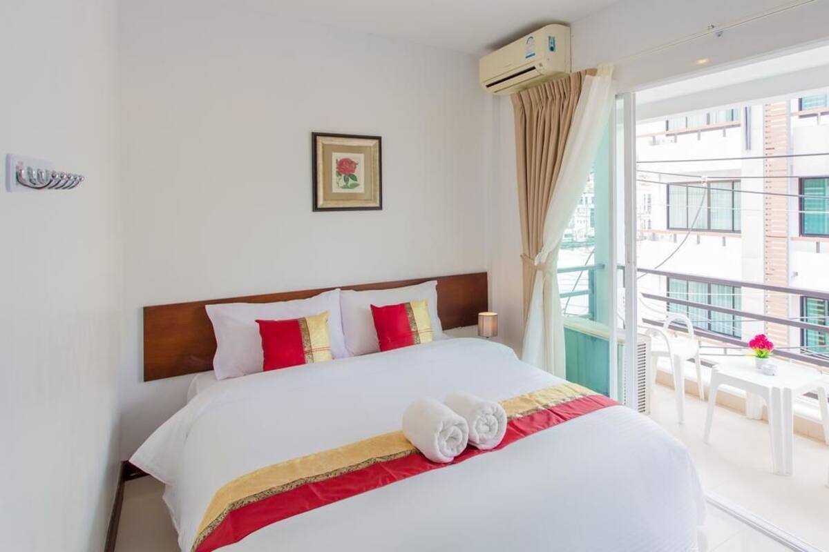 A hotel room with a large bed, a picture on the wall, an air conditioning unit, and a balcony with a table and chairs.