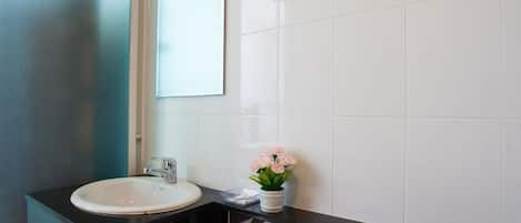 Un baño moderno con un lavabo blanco, encimera negra y un espejo encima.