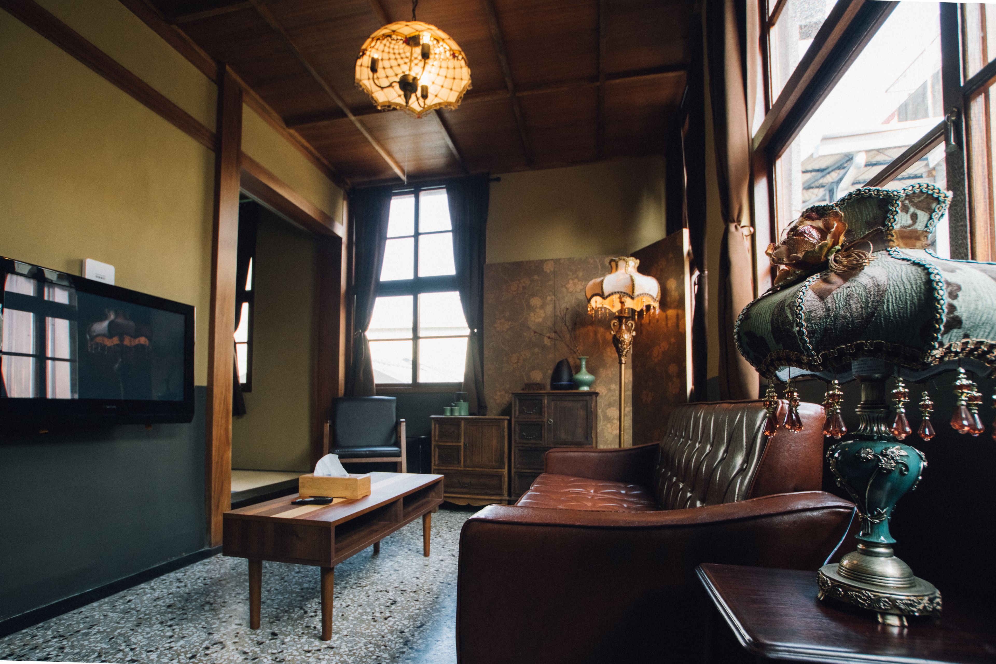A cozy room with a wooden ceiling, a leather sofa, a wooden table, a television, and a decorative lamp.