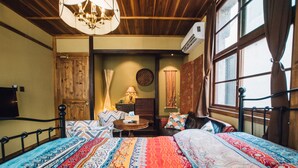 Una habitación con una cama grande, techo de madera, candelabro, ventana con cortinas y una pequeña mesa con lámpara.