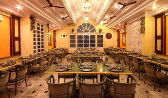 A large dining hall with multiple tables and chairs, ceiling fans, and a central arched window.