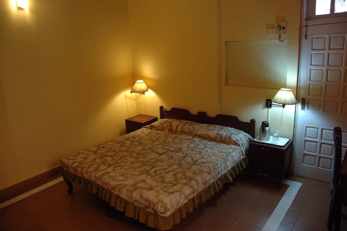 Une chambre à coucher avec un lit, deux tables de chevet, une commode, une lampe et une porte.