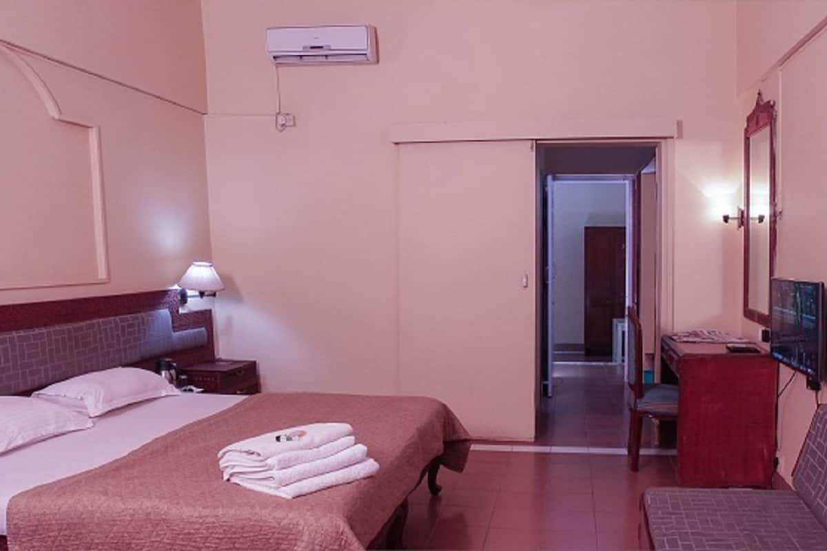 Une chambre d’hôtel avec un grand lit, un bureau avec une chaise, une télévision et une salle de bain visible à travers une porte ouverte.