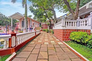 A pathway leading to a building with a red brick facade, white balustrades, and a covered area with a lamp post.