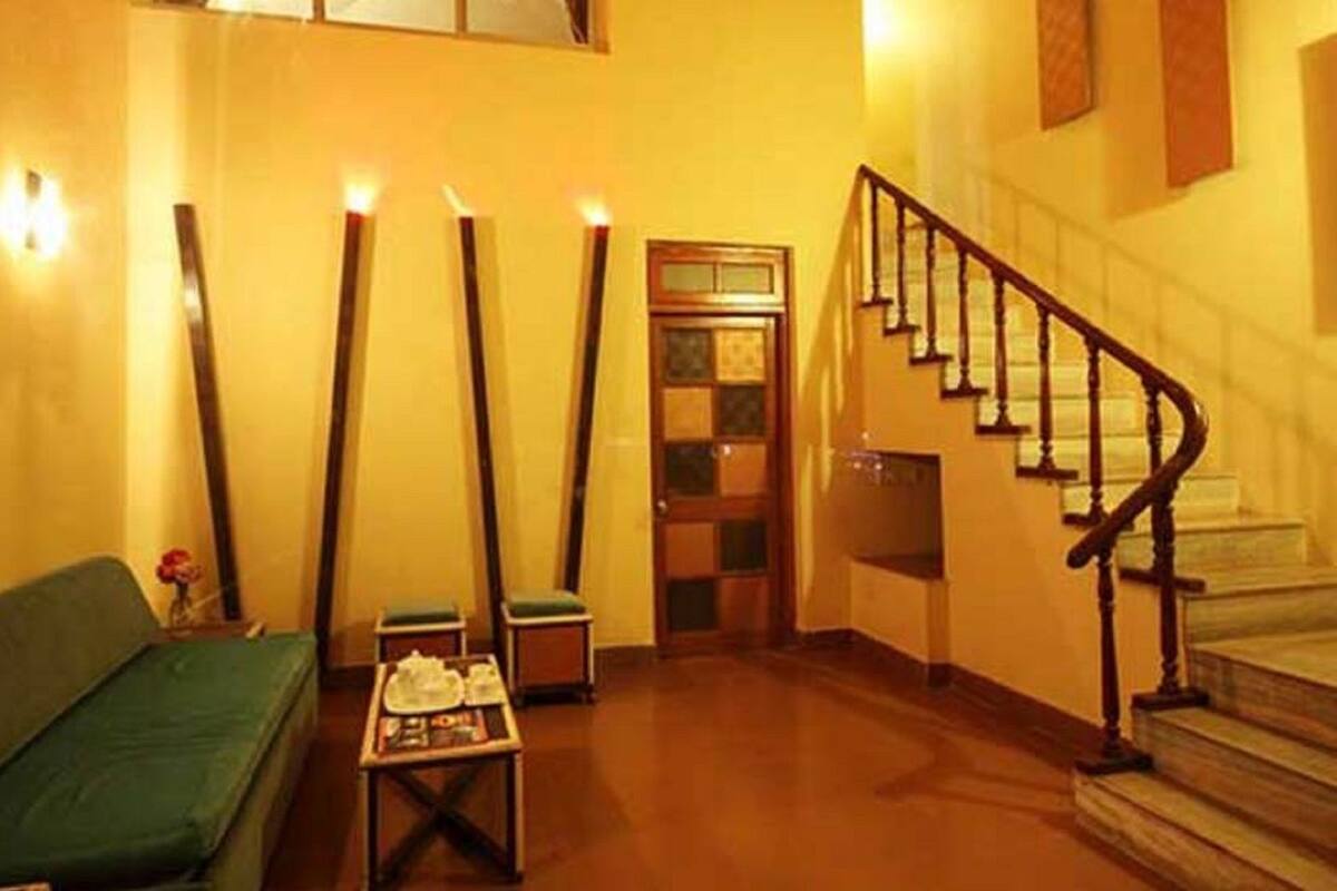 Un hall d’hôtel avec un canapé vert, une petite table sur laquelle sont posés divers objets, un escalier et une porte dotée de panneaux de verre.