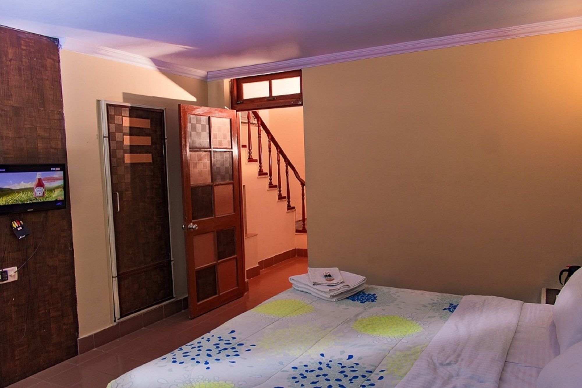 A bedroom with a bed, a television on the wall, a wooden door, and a staircase.