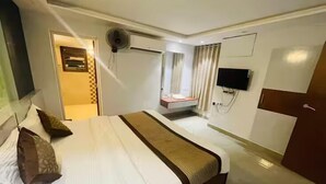 Een hotelkamer met een groot bed, een aan de muur bevestigde televisie en een zithoek met gordijnen.