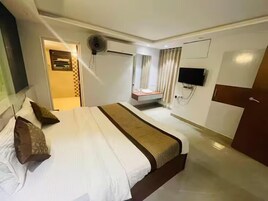 Habitación de hotel con una cama grande, un televisor montado en la pared y una pequeña zona de estar con cortinas.