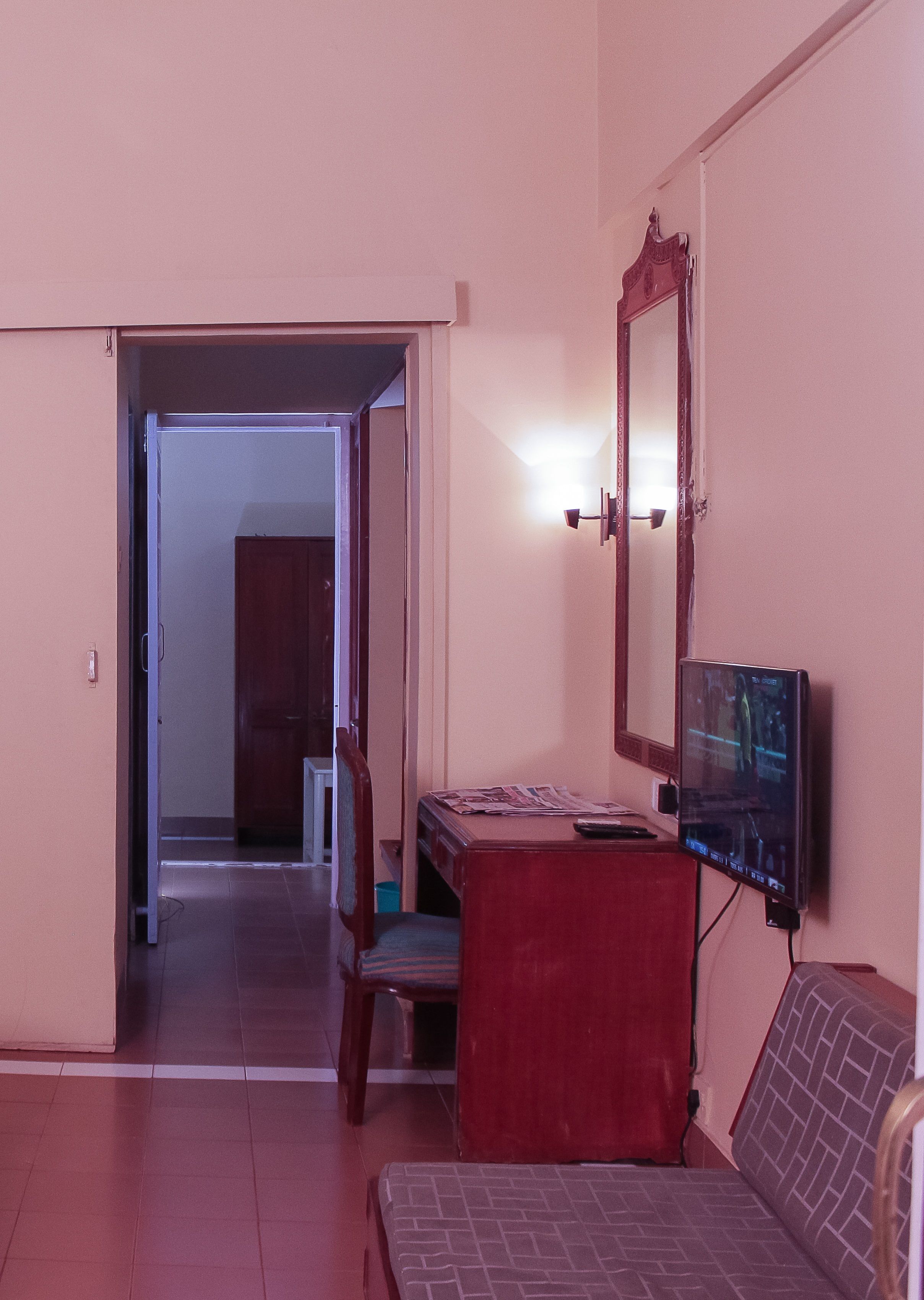 Um quarto com televisão, um armário vermelho, uma cadeira de madeira e uma cama.