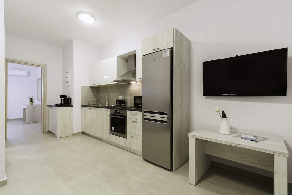 A modern kitchen with a built-in oven, a stainless steel refrigerator, and a flat-screen TV mounted on the wall.
