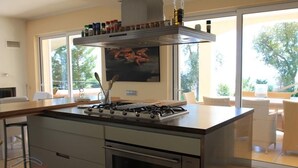 A modern kitchen with a gas stove, oven, and a large window overlooking a balcony. - Villa Mediterranea, Urb Rio de Oro (Calonge)