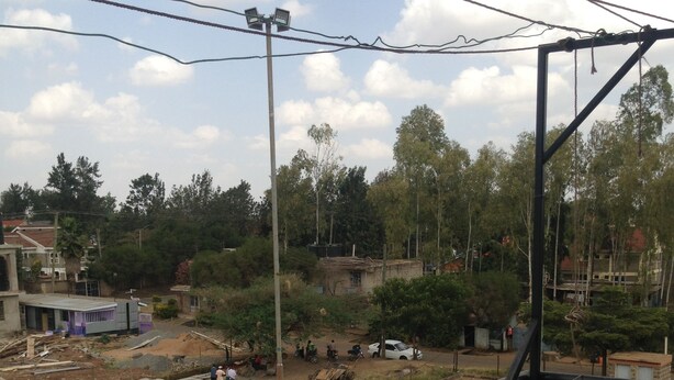 A balcony with a metal railing overlooking a construction site with vehicles and workers. - Tulos Apartment (Ruiru)