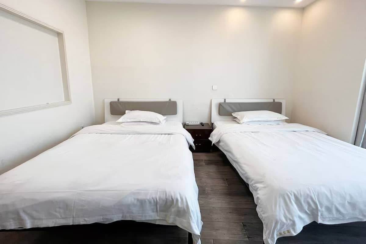 Una habitación con dos camas individuales, una mesita de noche con lámpara y una ventana.