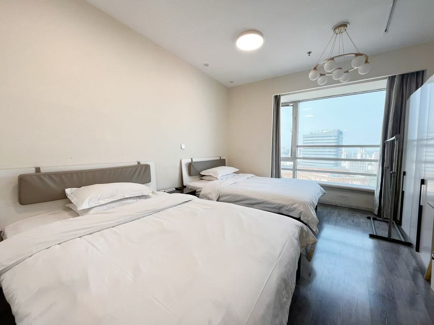 Et hotelværelse med to senge, et stort vindue med udsigt over byen, en loftlampe og en moderne lysekrone.
