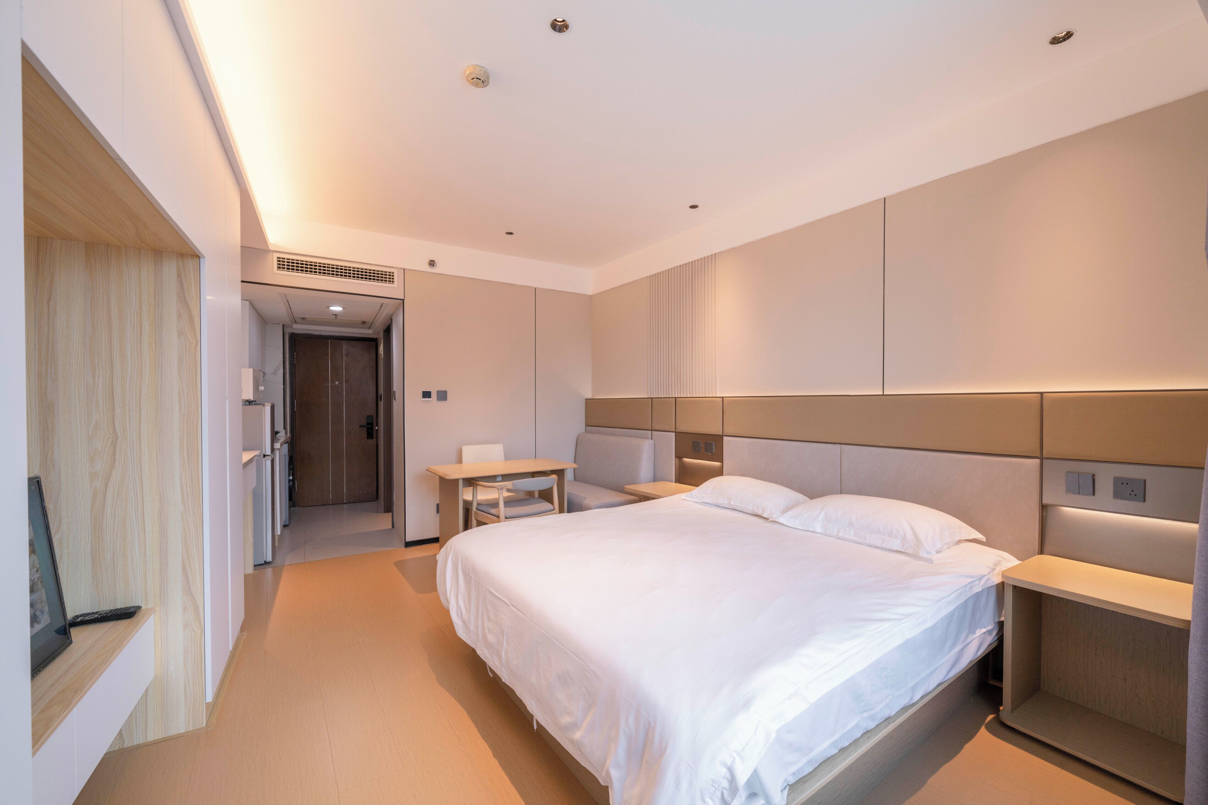 A modern hotel room with a large bed, bedside tables, a desk, and a wardrobe.