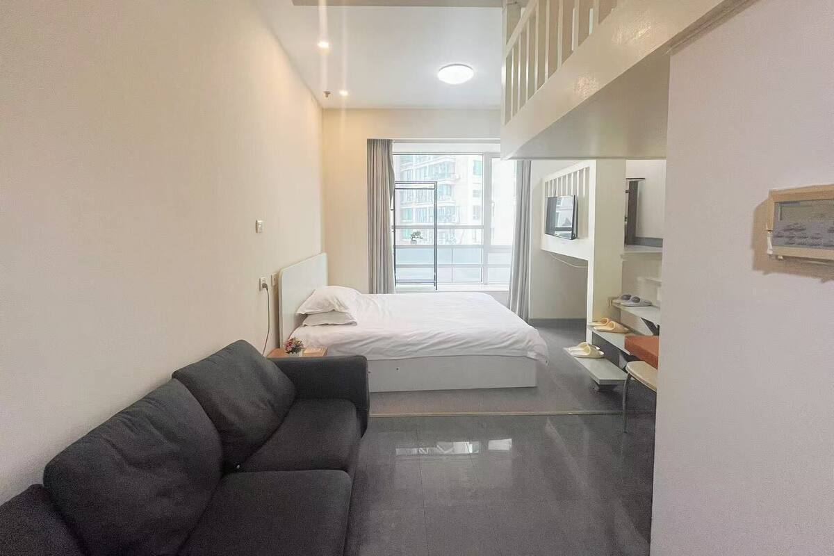 Habitación de hotel con cama, sofá, televisión y ventana con vista a edificios.