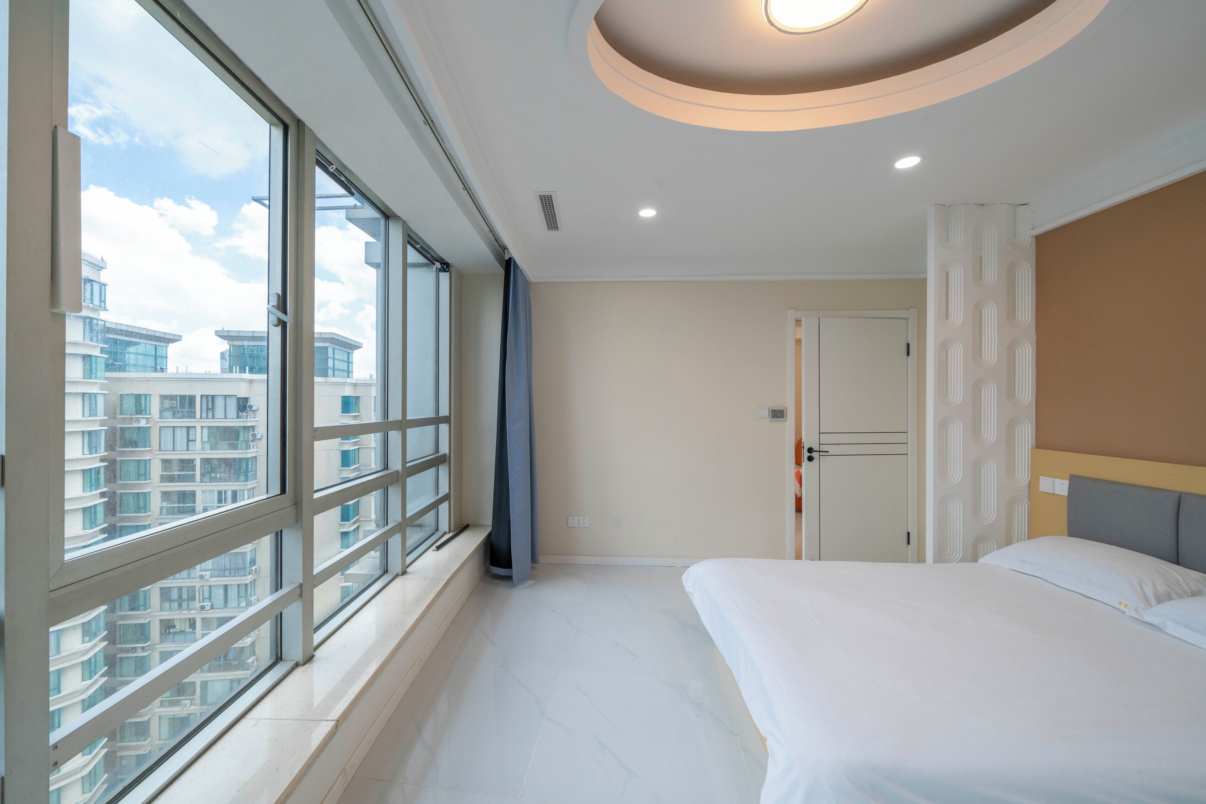 A hotel room with a large window, a bed, and a door.