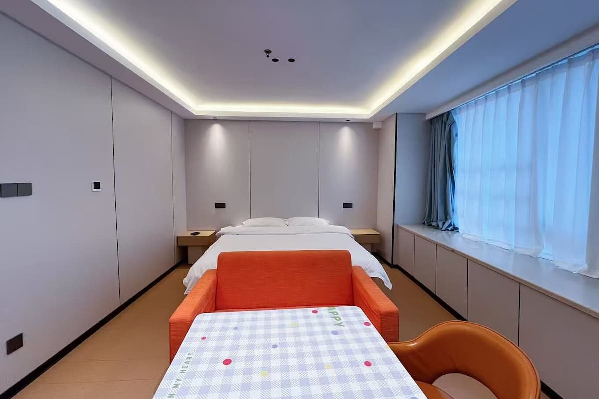 Una habitación de hotel con una cama, una mesa con mantel a cuadros, una silla y una ventana con cortinas.