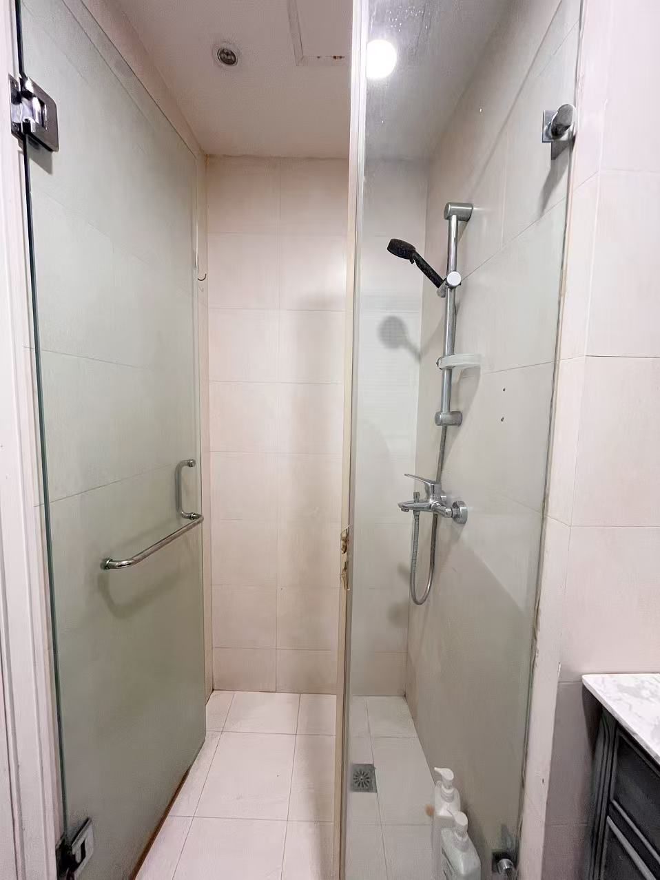 Een douchecabine met glazen wanden, een handdouche en een wandmengkraan.