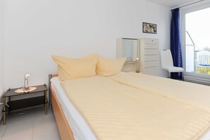 A neatly arranged bedroom with a bed, bedside table, dresser, and a chair near a window.