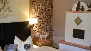 A hotel room with a bed, pillows, a wall with a log pattern, a lamp, and a small deer figurine. - Schrofenstube in the - Alpinrefugium Haus am Anger (Jungholz)