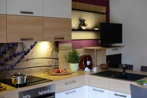 A modern kitchen with a built-in stove, a coffee maker, and a flat-screen TV mounted on the wall.