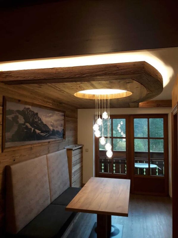 A wooden interior with a bench, a table, a hanging light fixture, and a window with a view.