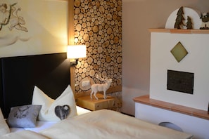 A hotel room with a bed, pillows, a wall with a log pattern, a lamp, and a small deer figurine. - Schrofenstube in the - Alpinrefugium Haus am Anger (Jungholz)