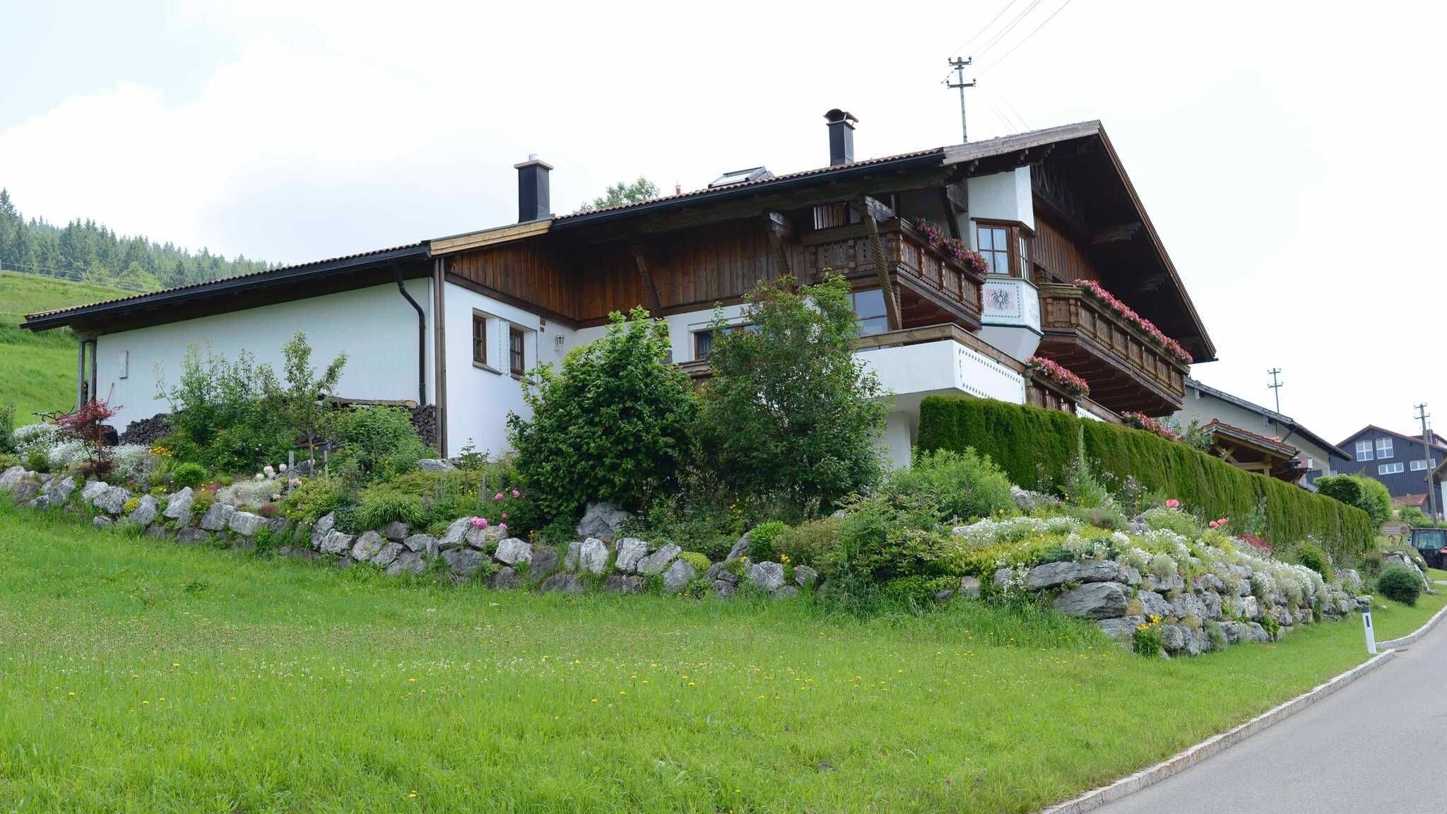 Una casa de estilo chalete tradicional con techo inclinado, balcones de madera y un muro de contención de piedra.