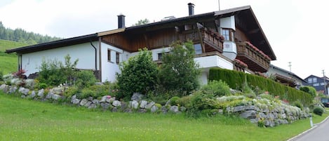Una casa de estilo chalete tradicional con techo inclinado, balcones de madera y un muro de contención de piedra.