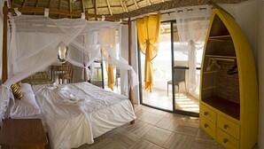 A bedroom with a bed, a wooden nightstand, a yellow armoire, and a balcony with yellow curtains. - Iris Island Eco Resort (Busuanga)