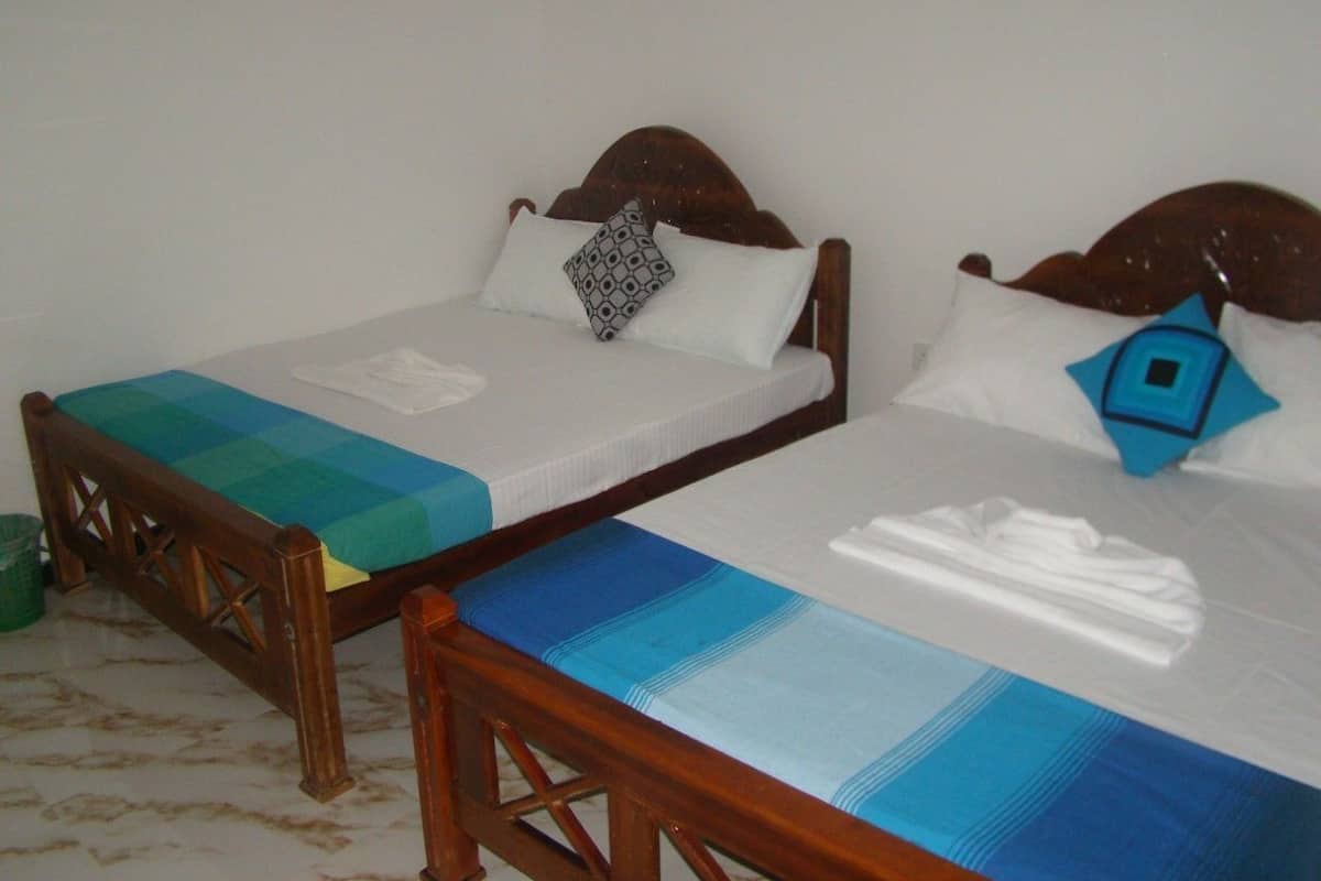 Two wooden beds with white mattresses and blue bedding, a green trash bin, and a wooden chair.