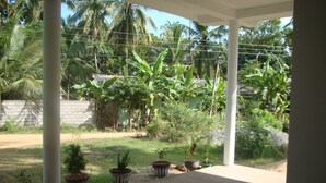 A covered outdoor area with potted plants and a concrete floor. - Nadun Rest (Polonnaruwa)