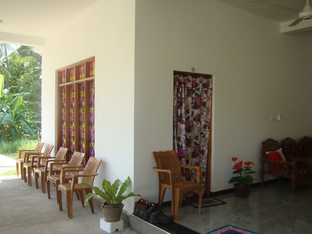 Ein Zimmer mit einer Reihe Holzsessel, einem Blumentopf und einer Tür mit floralen Vorhängen.
