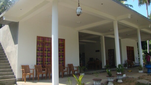 A covered outdoor area with a staircase, wooden chairs, and potted plants. - Nadun Rest (Polonnaruwa)