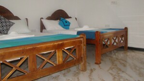 Two wooden beds with cross-bracing, white bedding, and a blue pillow. - Nadun Rest (Polonnaruwa)