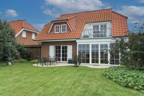 A two-story house with a red-tiled roof, a large glass door, and a patio with outdoor furniture.