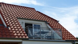 En bostadsbyggnad med ett rött tegeltak, ett väl synligt fönster och en balkong med metallräcken.