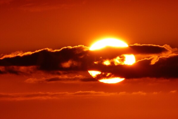 A sunset with the sun partially obscured by clouds.