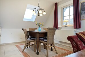 A dining area with a round table, four wicker chairs, a blue vase with flowers, and a chandelier.