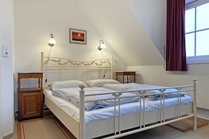 Un dormitorio con estructura de cama de metal blanco, dos mesitas de noche, una lámpara de pared e imagen enmarcada sobre la cama.