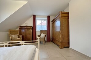 A bedroom with a bed, two wicker chairs, a wooden wardrobe, and a window with curtains.