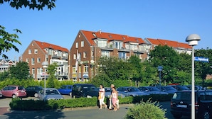 A parking lot with cars, a building with red roofs, and pedestrians walking. - Apartment Aurelia - Apartments in the North Sea Garden Park (Esens)