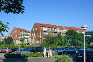 Un parking rempli de voitures, un bâtiment avec des toits rouges et des piétons qui se promènent.